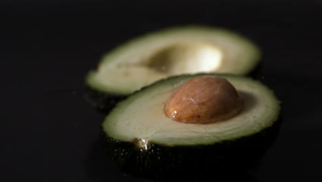 Wasser-Tropft-Auf-Avocadohälfte-Vor-Schwarzem-Hintergrund