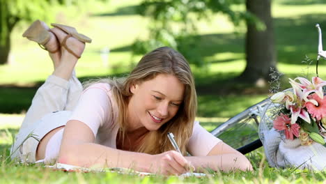 Una-Chica-Guapa-Escribiendo-En-Un-Bloc-De-Notas-Junto-A-Su-Bicicleta-En-El-Parque