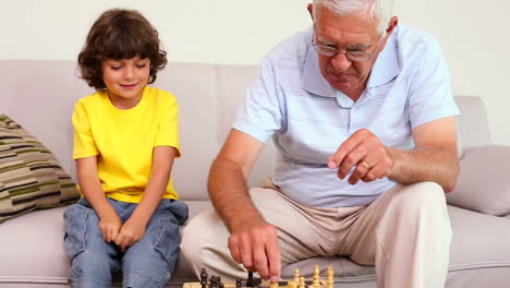 Senior-man-sitting-on-couch-with-his-grandson-playing-chess