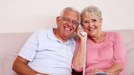 Senior-couple-sitting-on-sofa-talking-on-the-phone
