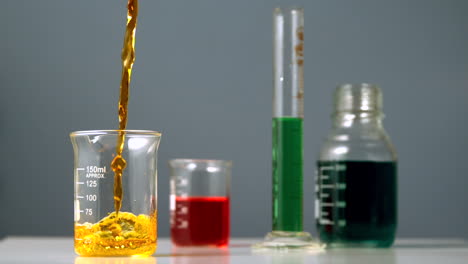 Orange-liquid-pouring-into-beaker-on-chemists-table