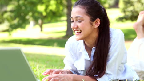 Una-Chica-Guapa-Tirada-En-El-Césped-Usando-Su-Computadora-Portátil