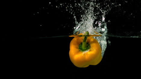 Yellow-pepper-falling-in-water-on-black-background