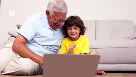 Senior-man-sitting-on-floor-with-his-grandson-using-laptop