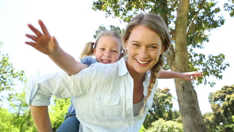 Glückliches-Kleines-Mädchen-Bekommt-Im-Park-Ein-Huckepack-Von-Der-Mutter