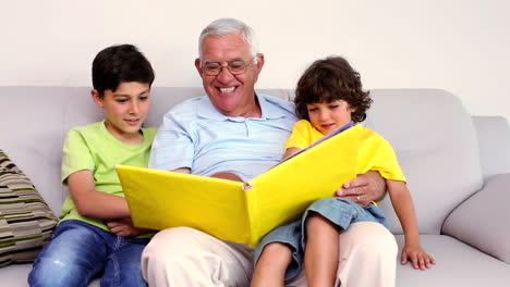 Älterer-Mann-Sitzt-Mit-Seinen-Enkeln-Auf-Der-Couch-Und-Schaut-Sich-Ein-Fotoalbum-An