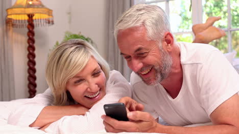Couple-lying-on-bed-using-smartphone-together