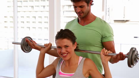 Fit-woman-lifting-barbell-with-help-of-trainer