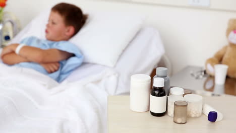 Little-sick-boy-sitting-in-bed-with-medicine-in-foreground