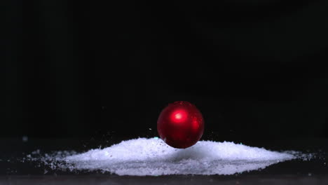 Christmas-bauble-falling-onto-pile-of-glitter-on-white-background