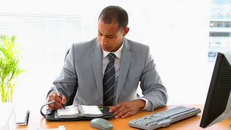 Businessman-working-at-his-desk-and-writing-in-diary