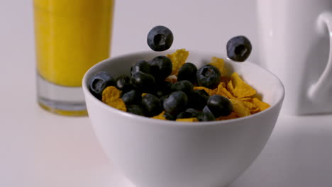 Blueberries-pouring-into-cereal-bowl-at-breakfast-table