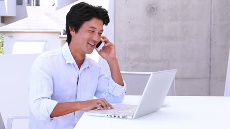 Asian-man-using-laptop-and-answering-his-phone