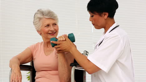 Nurse-talking-with-elderly-patient-in-a-wheelchair-lifting-a-dumbbell