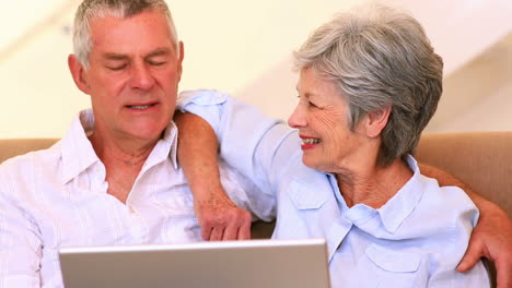 Feliz-Pareja-De-Ancianos-Sentados-En-El-Sofá-Usando-Una-Computadora-Portátil
