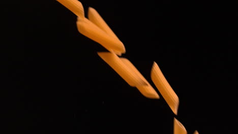 Penne-pasta-pouring-against-black-background