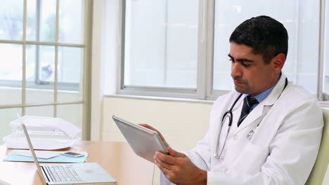 Doctor-sitting-at-desk-using-tablet-pc