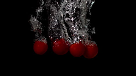 Cherry-tomatoes-falling-in-water-on-black-background
