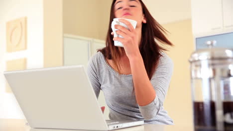 Pretty-brunette-sitting-using-laptop-and-drinking-coffee