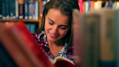 Pretty-student-reading-book-standing-in-the-library