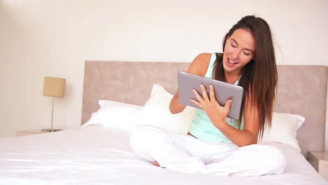 Pretty-brunette-sitting-on-bed-using-her-tablet
