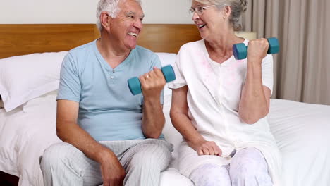 Senior-couple-sitting-on-bed-lifting-dumbbells