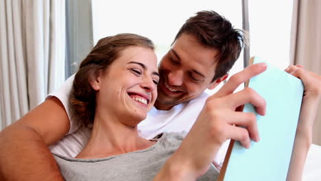 Happy-couple-lying-on-bed-reading-together