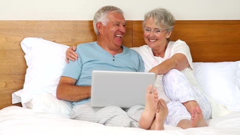 Senior-couple-sitting-on-bed-using-laptop
