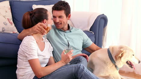 Glückliches-Paar-Sitzt-Auf-Dem-Boden-Und-Trinkt-Wein-Mit-Ihrem-Hund