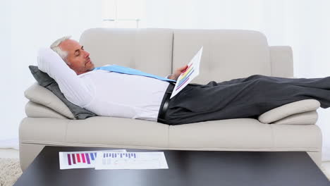 Businessman-falling-asleep-holding-paperwork-on-the-couch