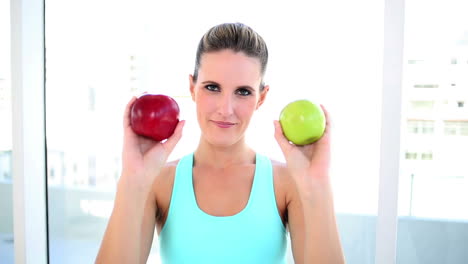 Smiling-fit-woman-showing-two-apples
