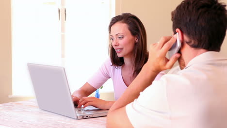 Frau-Benutzt-Laptop-Mit-Partner-Und-Telefoniert-Am-Tisch