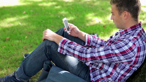 Apuesto-Joven-Estudiante-Sentado-En-El-Césped-Enviando-Mensajes-De-Texto