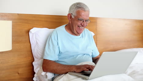 Älterer-Mann-Sitzt-Im-Bett-Mit-Laptop