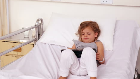 Little-girl-lying-in-hospital-bed-using-a-tablet