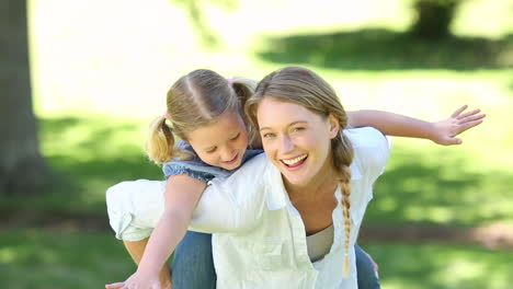 Happy-little-girl-getting-a-piggy-back-from-mother-in-the-park