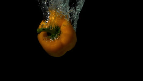 Yellow-pepper-falling-in-water-on-black-background