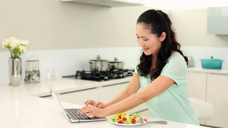 Smiling-woman-using-laptop-and-eating-salad