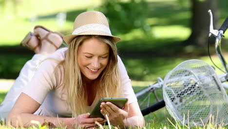 Pretty-girl-using-tablet-pc-beside-her-bike-in-the-park