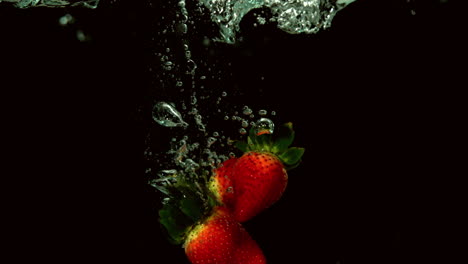 Strawberries-falling-in-water-on-black-background