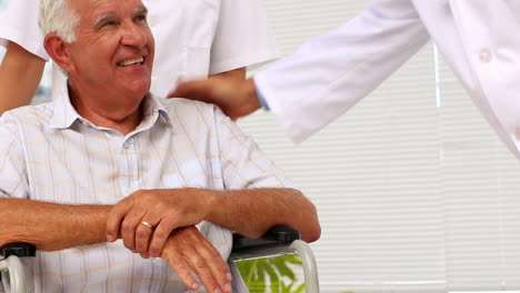 Doctor-talking-with-elderly-patient-in-a-wheelchair-being-pushed-by-nurse