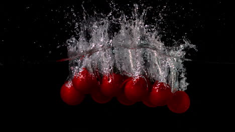 Cherry-tomatoes-falling-in-water-on-black-background