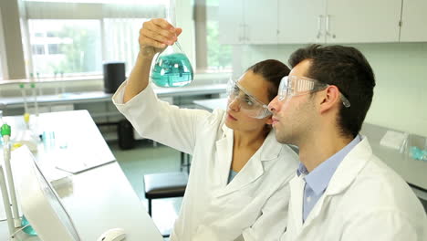 Science-students-looking-at-blue-chemical-together-using-computer