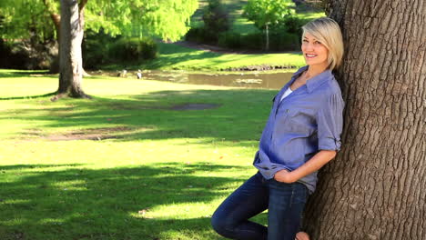 Smiling-woman-leaning-against-a-tree