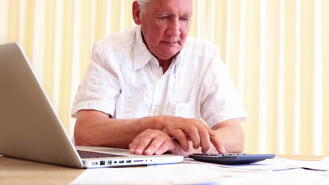 Älterer-Mann-Sitzt-Am-Tisch-Und-Bezahlt-Mit-Seinem-Laptop-Seine-Rechnungen