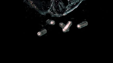 White-pills-falling-in-water-on-black-background