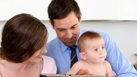 Happy-parents-using-tablet-pc-with-their-baby-son-in-the-morning