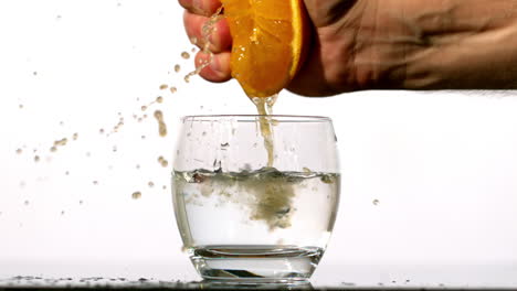 Hand-squeezing-juice-of-orange-into-glass-of-water