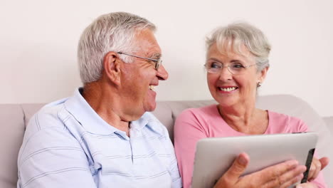 Senior-couple-sitting-on-sofa-using-tablet-pc
