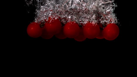 Cherry-tomatoes-falling-in-water-on-black-background